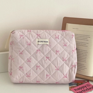 Détail d'une trousse à maquillage matelassée rose avec motifs nœuds et logo de marque
