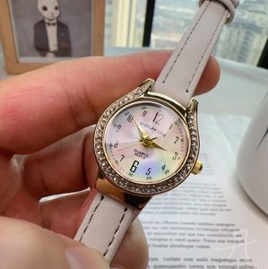 Close-up of women's quartz watch with rhinestone gold case and white leather strap