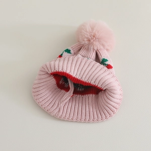 Detail of pink knitted baby hat with cherry embroidery and fluffy faux fur pom-pom