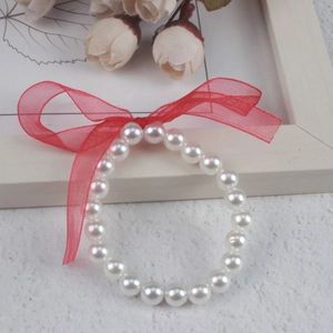 Close-up of white faux pearl bracelet with a red tulle bow on a rustic desk