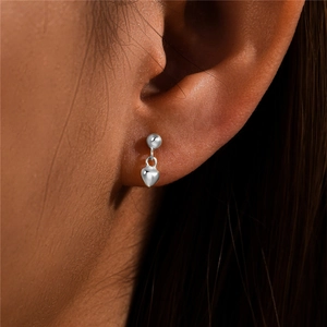 Detailed view of a silver heart-shaped pendant earring worn on an ear cartilage