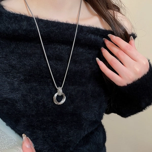 Close-up of layered silver multi-ring pendant on a sleek snake chain over black fabric
