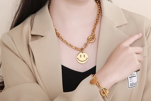 Detail of gold thick chain necklace and bracelet set with smiley face and toggle clasp