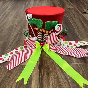 Detail of red plush Christmas tree topper hat with elf legs and green glitter bow