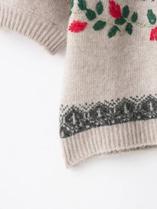 Detail of oatmeal knit sweater with red floral embroidery and ribbed hem craftsmanship