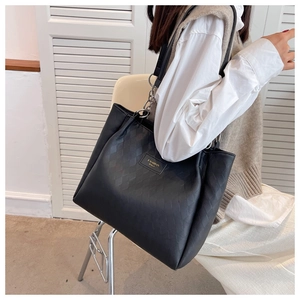 Detail of black quilted tote bag featuring a gold chain and textured rhombus pattern
