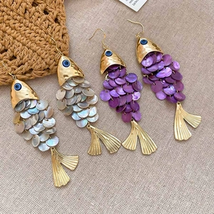 Detailed view of fish-shaped earrings with layered iridescent shells and gold metal fins