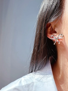 Detailed close-up of a silver bow earring with shimmering stones worn on an ear