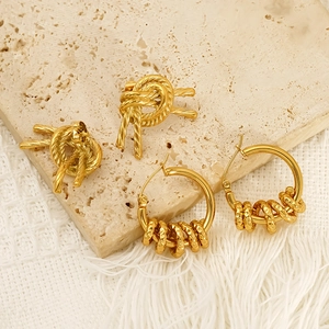 Golden woven knot studs and textured hoop earrings set on elegant beige stone display