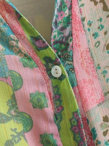 Détail de robe à col en V avec imprimé coloré, fils dorés et un bouton rond blanc