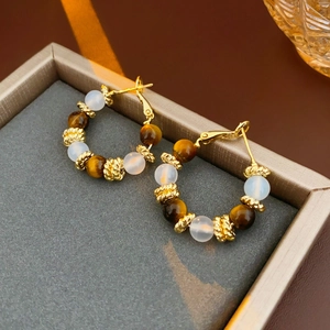 Detailed shot of gold-plated hoop earrings with tiger eye and milky white beads