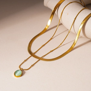 Détail d'un collier doré double épaisseur avec chaîne serpent et pendentif en pierre oeil de chat