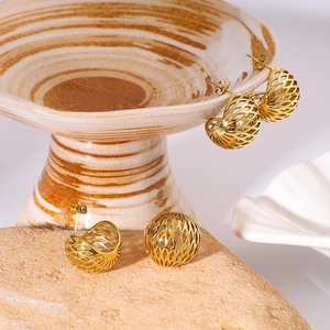 Golden hollow mesh sphere earrings made of stainless steel displayed on a stone and bowl