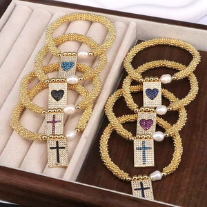 Detail of gold beaded bracelets with heart and cross charms and shimmering zircon stones