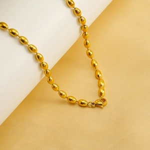 Detailed close-up of golden oval bead necklace with lobster clasp on silk fabric