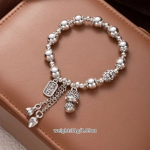 Detail view of silver bead bracelet with Buddha and lotus charms on brown leather background