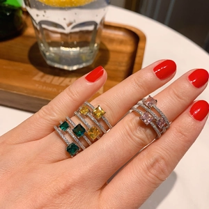Detail of square-cut pink and emerald green gemstones on layered silver ring bands