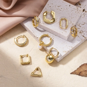 Golden geometric earrings set with pearls and zircons displayed on natural stone