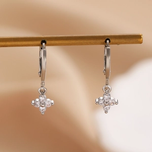 Macro shot of silver flower earrings with white zircon stones on a gold display stand