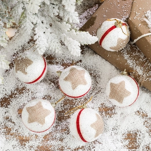 White foam Christmas ball with red ribbon and burlap star on snowy wood base
