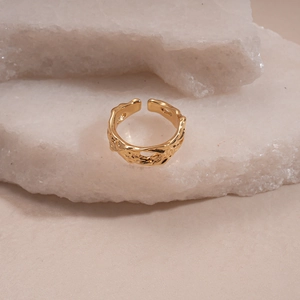 Detailed close-up of a gold-toned hammered texture open ring on white stone background