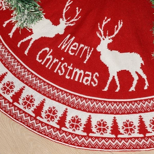 Knitted red and white Christmas tree skirt with reindeer pattern on wooden floor