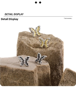 Macro detail of gothic butterfly stud earrings in black and gold on textured rocks