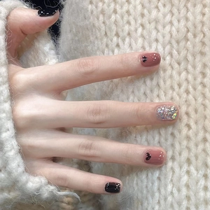 Close-up of pink press-on nails with black heart patterns and silver glitter accents