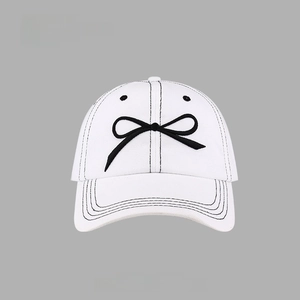 Close-up of a white cotton baseball cap featuring detailed black bow-tie embroidery