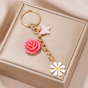 Gold keychain with pink resin rose, butterfly and daisy charms on a jewelry box