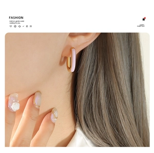 Close-up of model wearing U-shaped gold earrings with pink and purple enamel finish