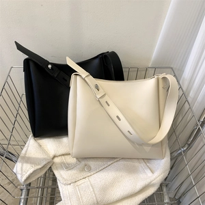 Detail of minimalist bucket tote bags in black and cream leather inside a wire basket