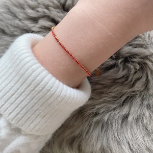 Macro shot of minimalist red braided bracelet with gold beads worn on a wrist