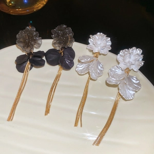 Macro view of elegant flower petal tassel earrings with gold chains on a ceramic tray