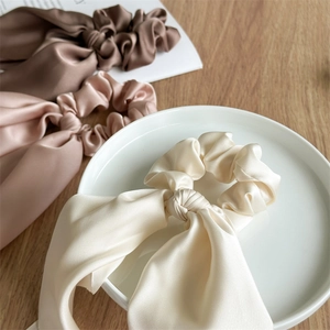 Three silk satin scrunchies with long ribbons in beige, pink and brown on a desk