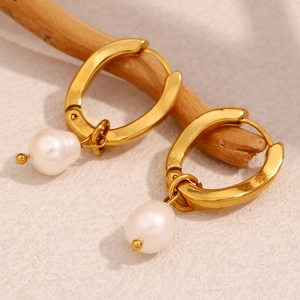 Macro view of gold plated U-shaped earring with dangling baroque white pearl on wood