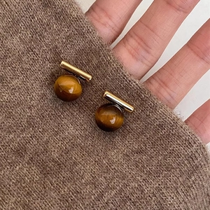 Détail de boucles d'oreilles boule en oeil de tigre doré sur un pull en maille marron