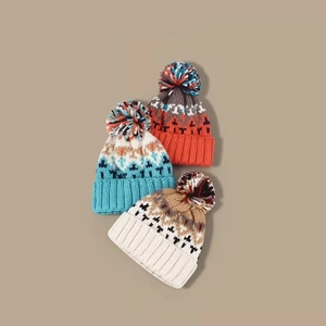 Three warm knit beanies with colorful pom poms and geometric patterns in various colors