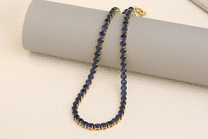 Detail of 18K gold-plated tennis necklace with claw-set deep blue round gemstones