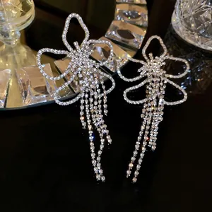 Sparkling silver bow knot long fringe earrings with crystals on a black reflective surface