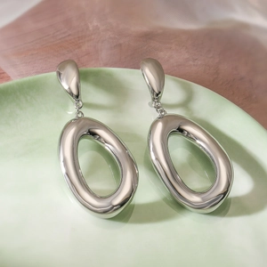 Detailed view of silver oval drop earrings on green ceramic plate with metallic shine