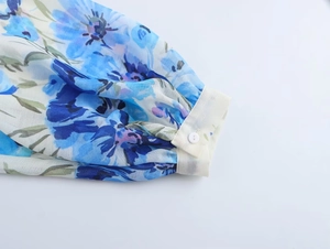Dettaglio del polsino di camicetta in chiffon floreale con bottone beige e manica a lanterna