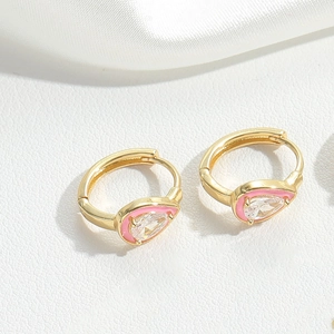 Close-up of gold earrings featuring pink enamel and a teardrop clear gemstone on silk