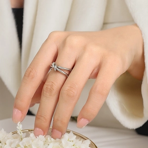 Close-up of double-line knotted stainless steel ring worn on finger with floral background