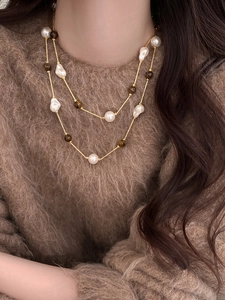 Close-up of double-layer necklace with tiger eye stone and pearls on camel wool sweater