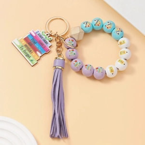 Detail of beaded teacher keychain with purple tassel and engraved wooden book pendant