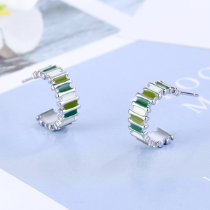 Close-up of C-shaped earrings with green and white enamel on silver metal base