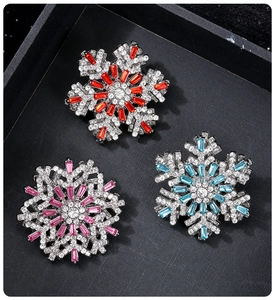 Detailed macro view of three crystal snowflake brooches in red, pink, and blue gemstone centers