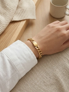 Close-up of a chunky gold Cuban link bracelet with a polished metal plate on a woman's wrist