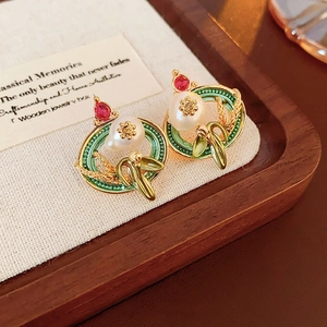 Detailed shot of vintage gold earrings with green enamel leaves, pearls and red gems